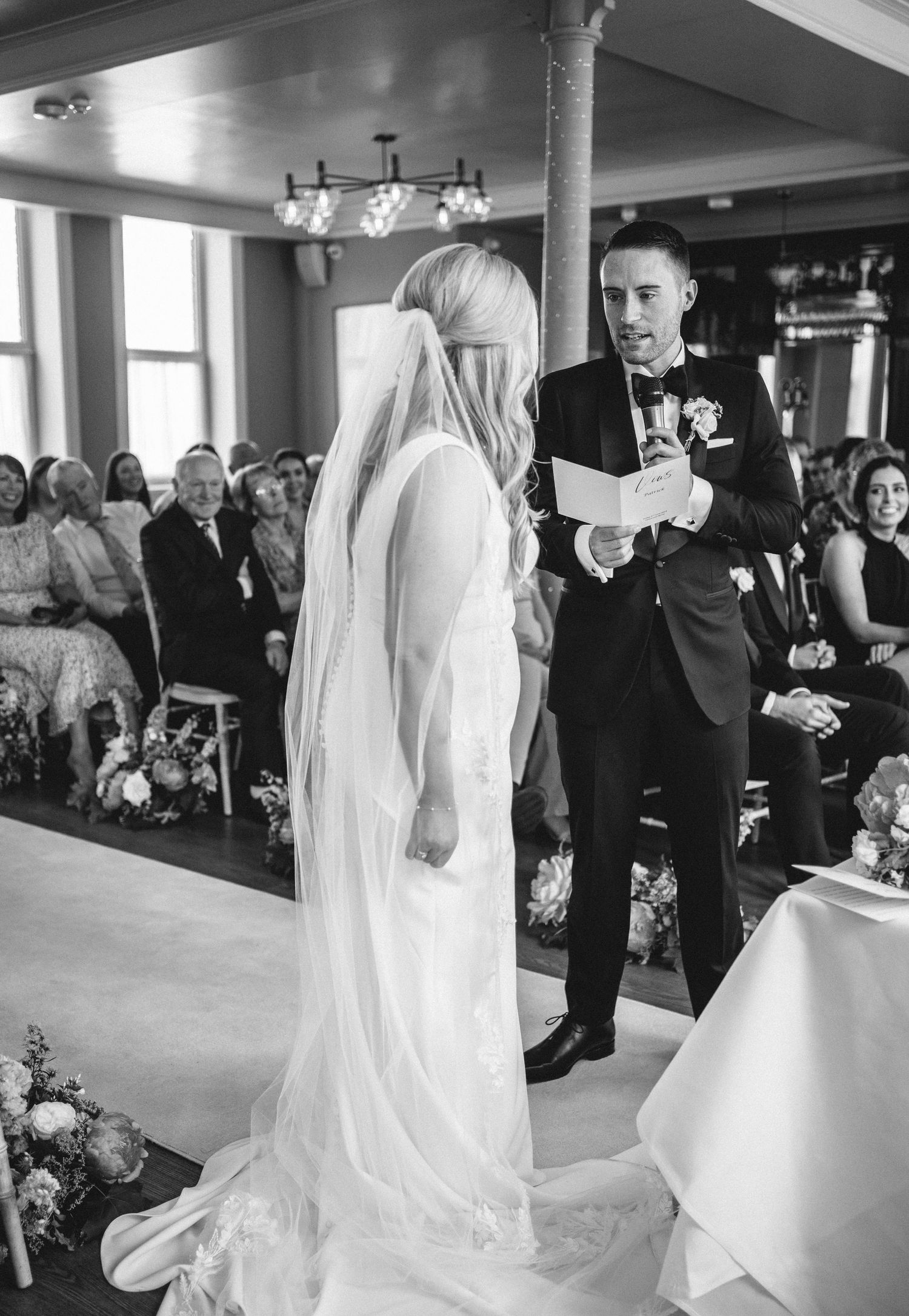 A couple exchanges vows during their wedding ceremony in front of seated guests in an elegant indoor venue.