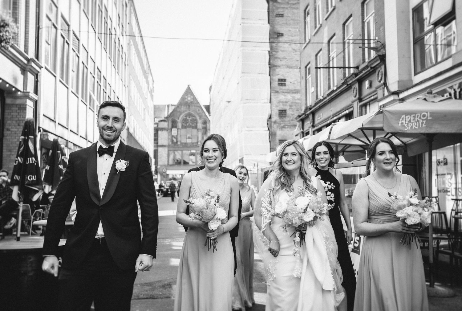 Black and white photo of wedding party walking down city street with historic architecture.