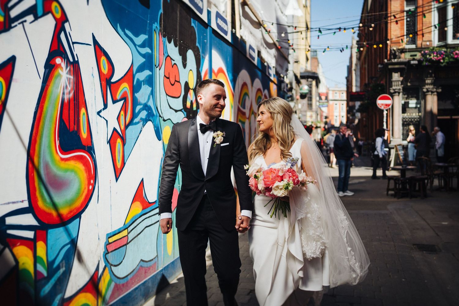 Newlyweds walk together past colorful street art murals on their urban wedding day celebration.