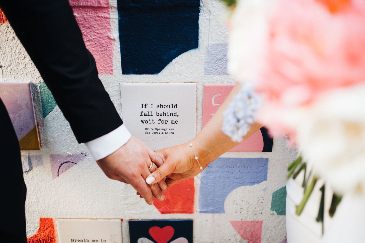 Close-up shot of a couple holding hands against a colorful mural wall.