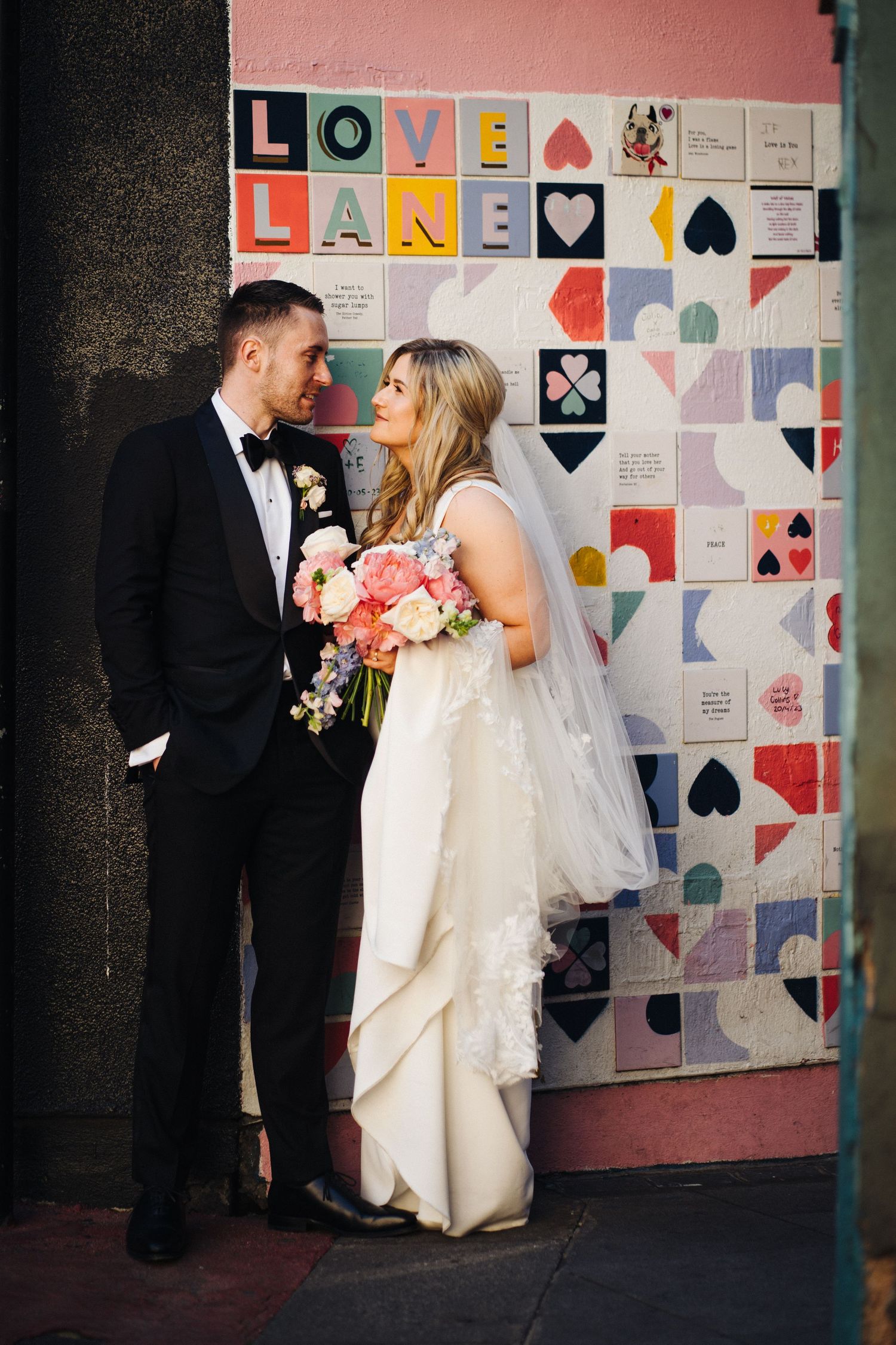 Wedding couple poses against colorful geometric wall art with text reading 'Love Lane'.