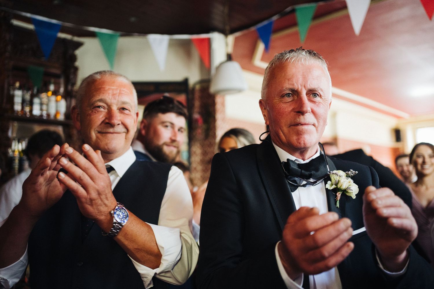 Wedding guests in formal attire applauding during reception celebration.