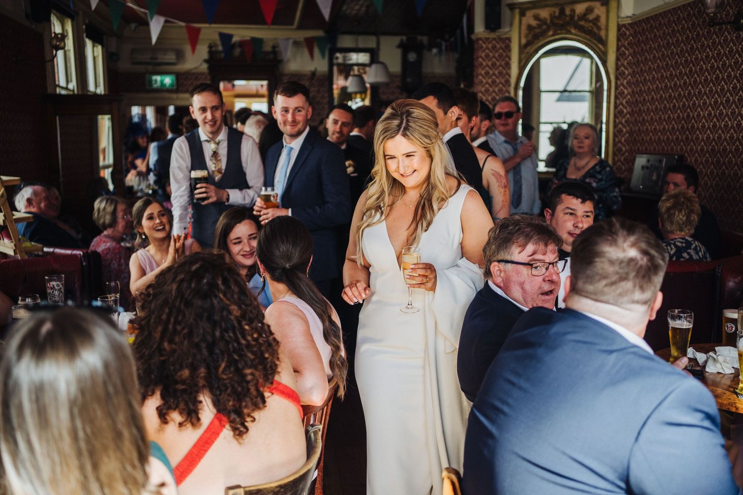 Wedding reception scene with guests celebrating in a pub decorated with colorful bunting.