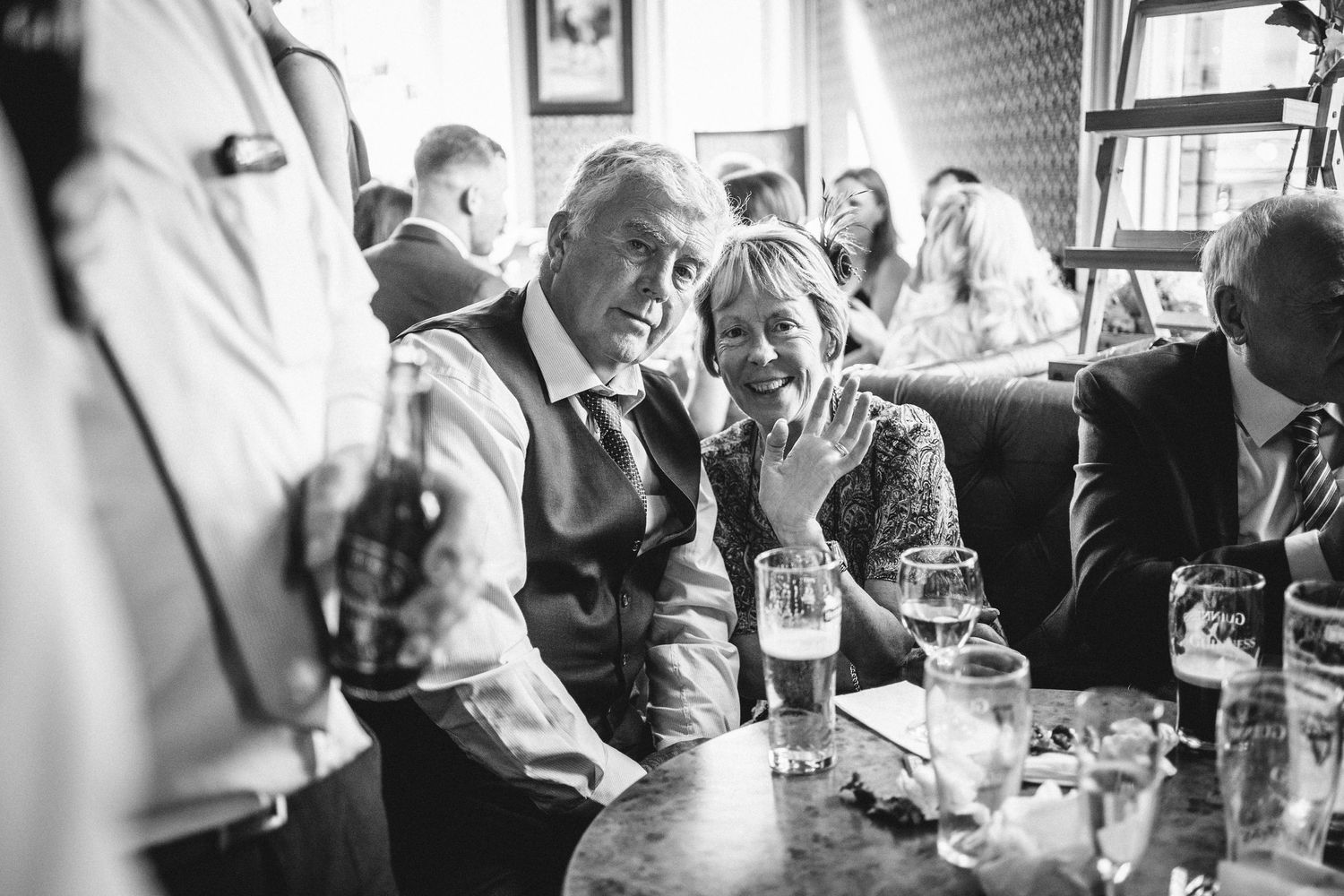 Black and white photo of guests enjoying drinks and conversation at a pub gathering.