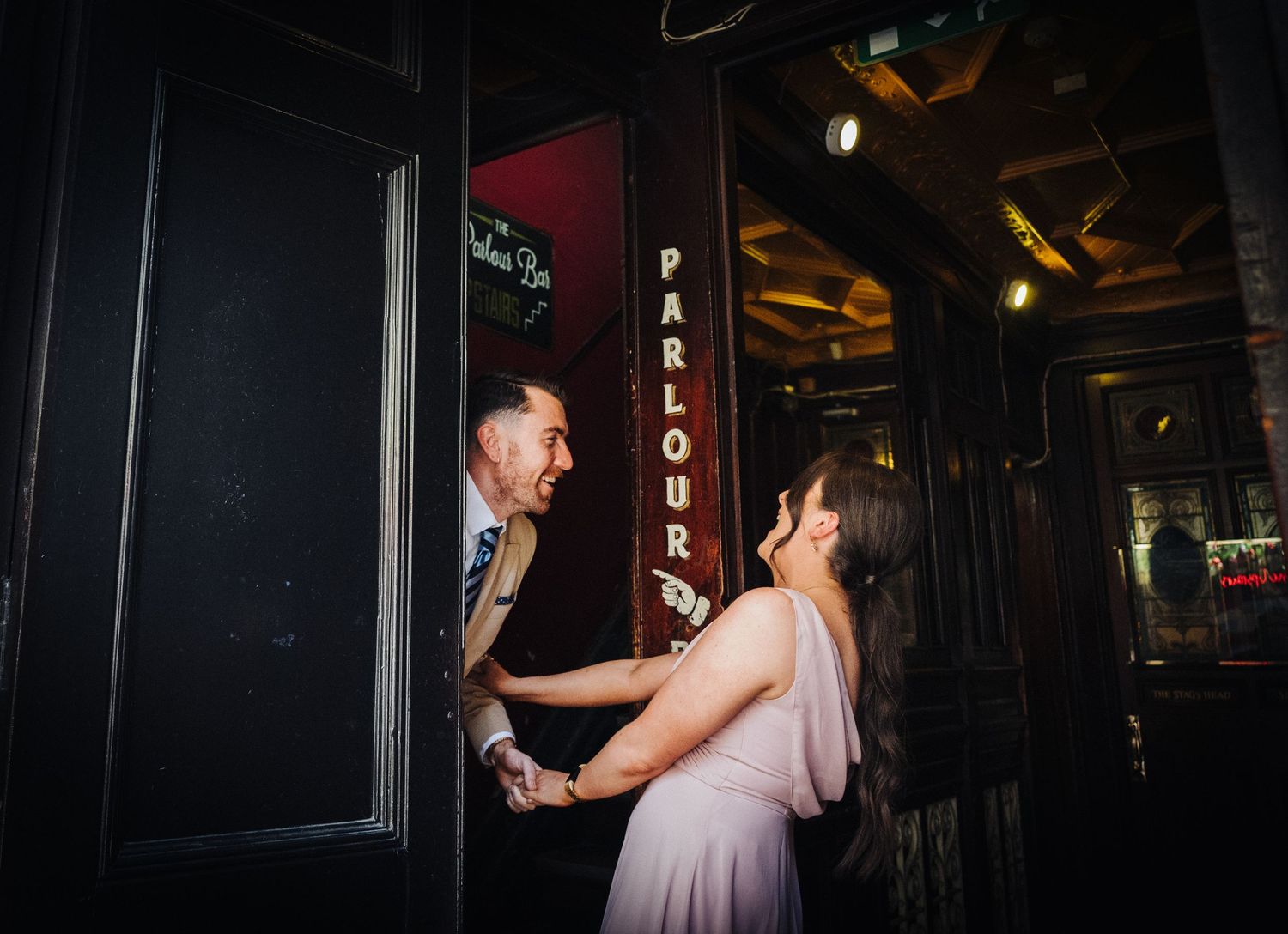 A couple shares a joyful moment by a doorway in a dimly lit venue.