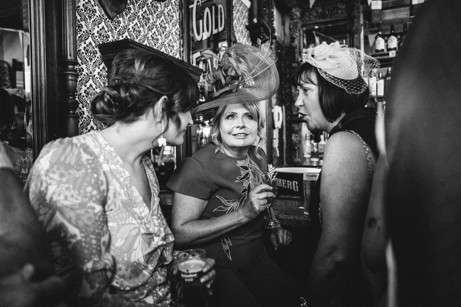 Black and white photo shows guests sharing drinks and stories in a vintage pub setting.