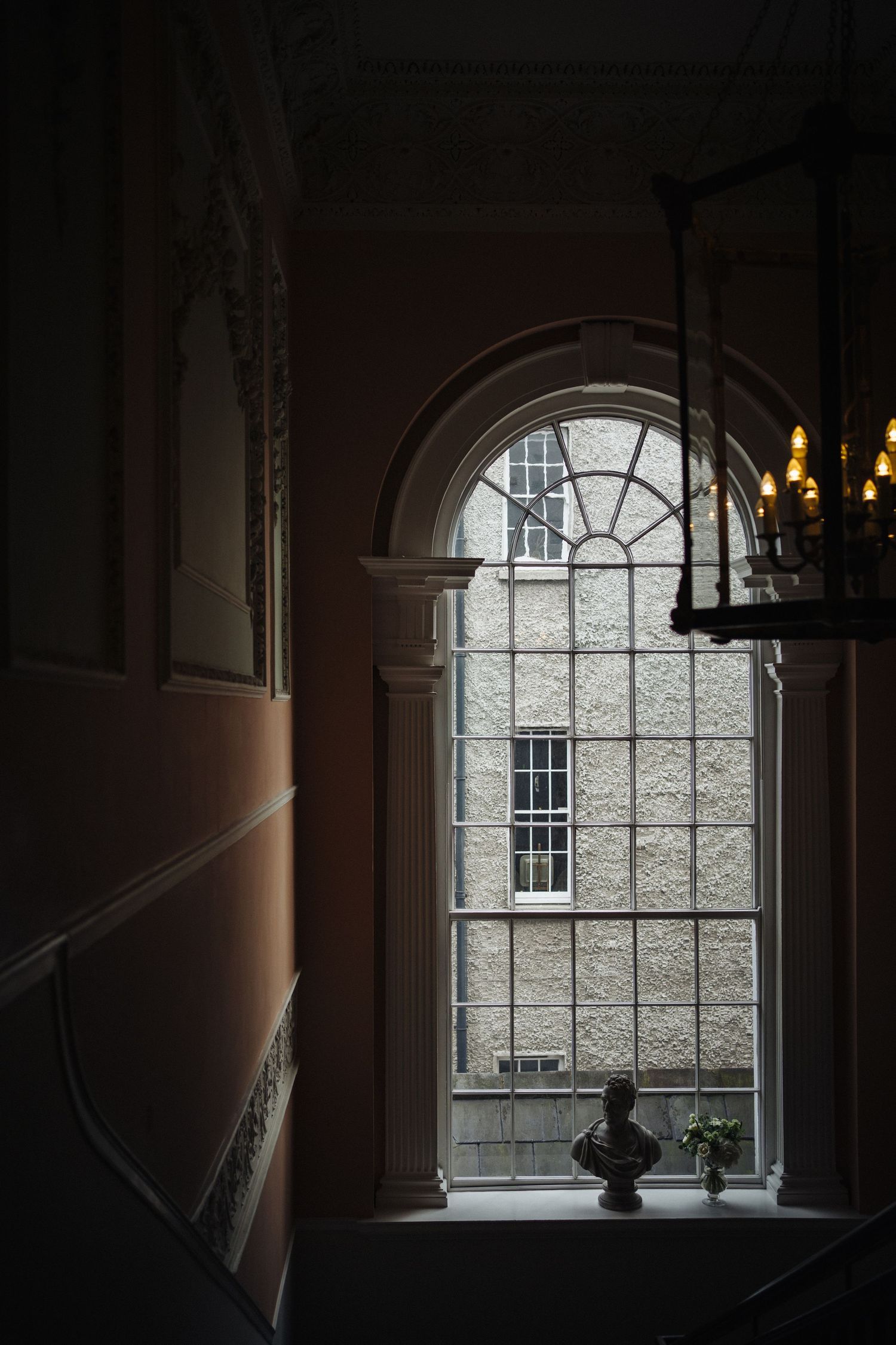 Arched window in dark hallway frames view of historic stone building exterior.