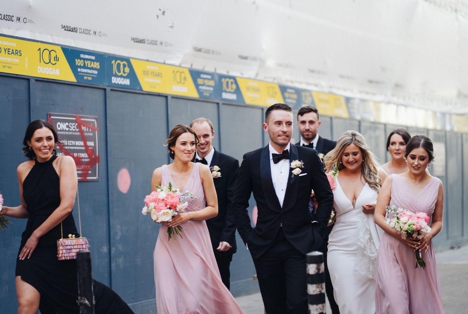 Wedding party walks together outside with bridesmaids in pink dresses carrying bouquets.