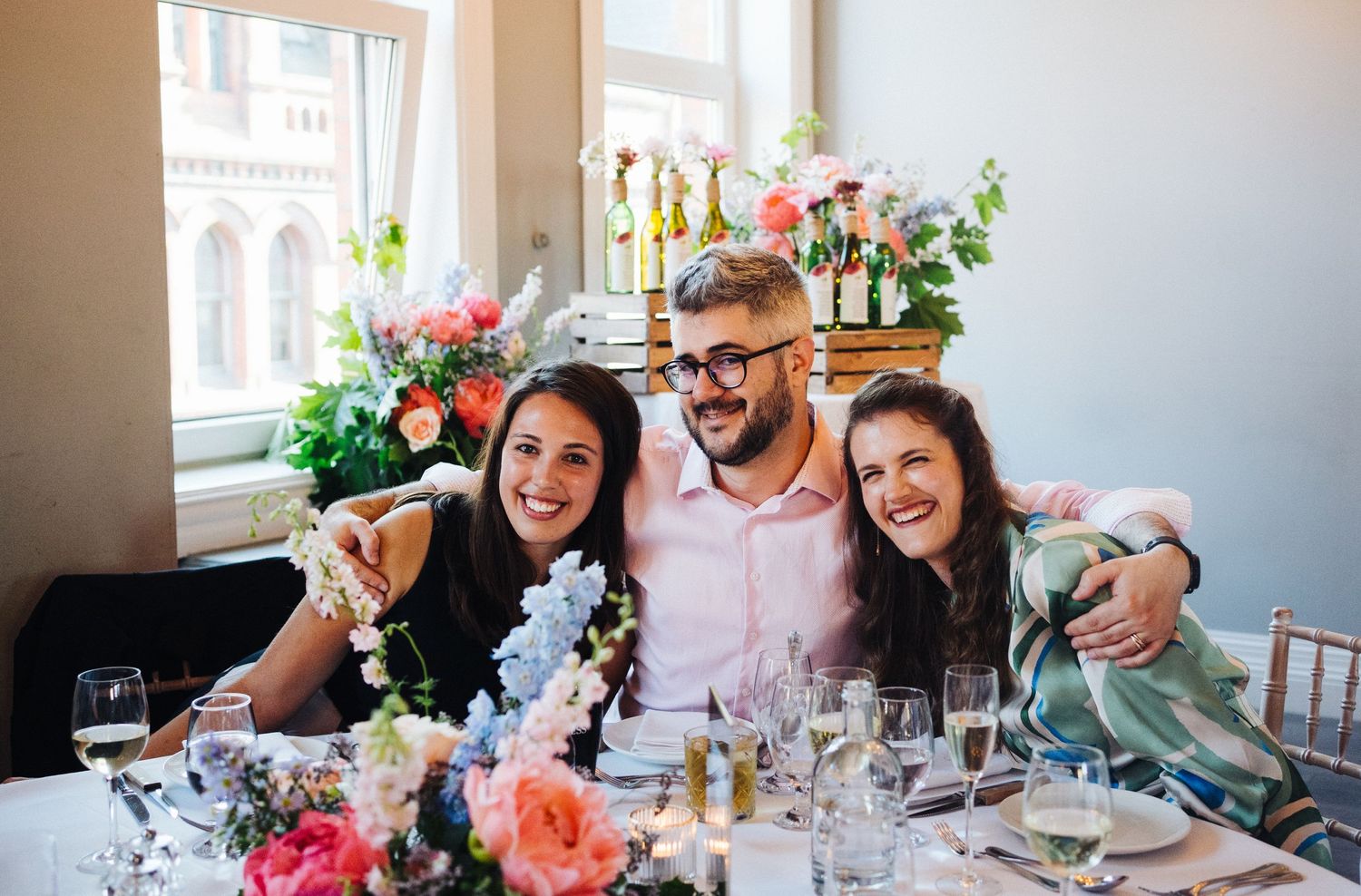Reception guests celebrate at decorated table with pink flowers and champagne glasses.