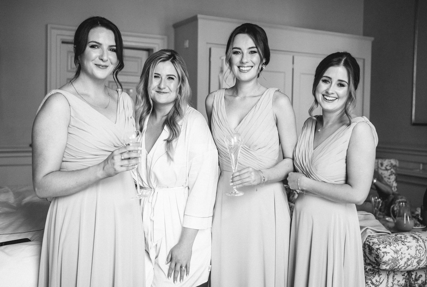 Group photo of bridesmaids wearing light colored dresses in an elegant room.