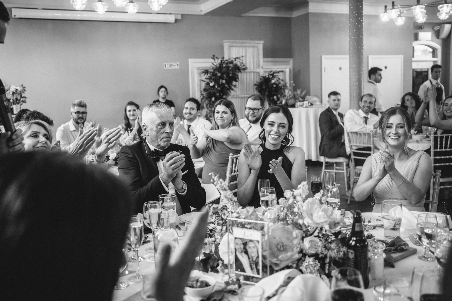 Wedding guests react emotionally to speeches during an indoor reception with floral decorations.