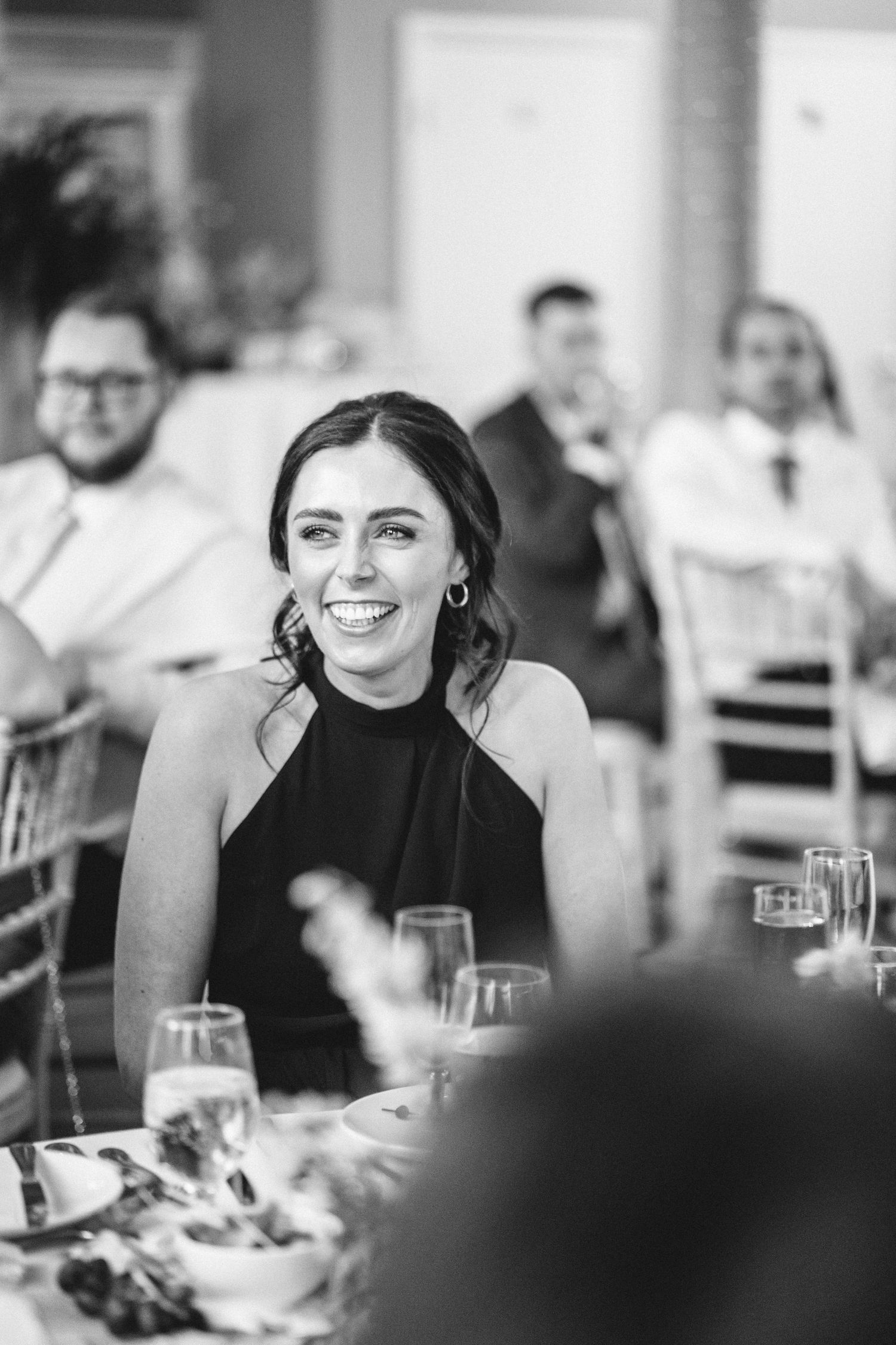 A guest in a black dress smiles during a wedding reception celebration.