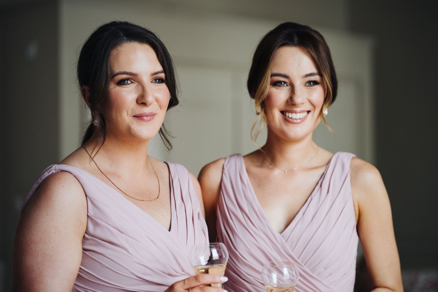 Two bridesmaids in matching dusty rose dresses share a moment together.