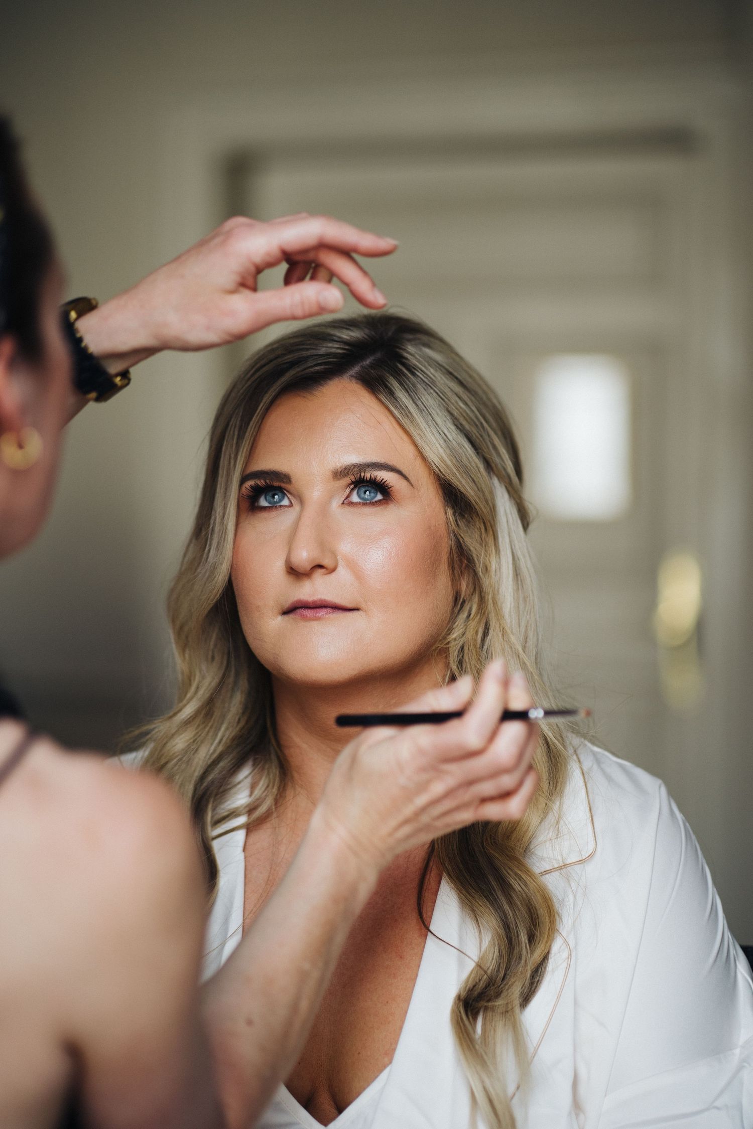 Professional makeup artist applying delicate touches to a bride's face during wedding day preparations.