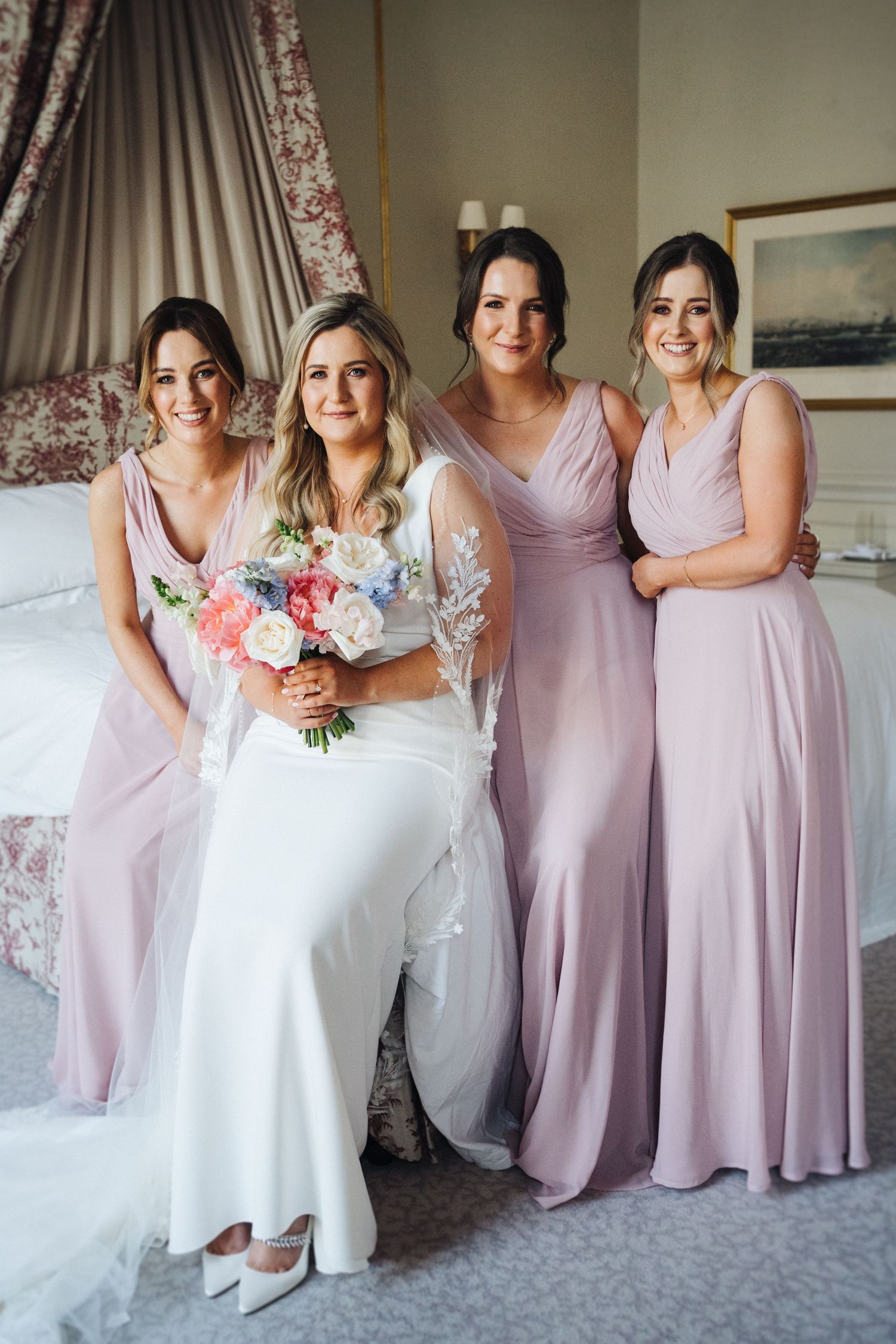 Bridal party poses together in pink bridesmaid dresses and white wedding gown.