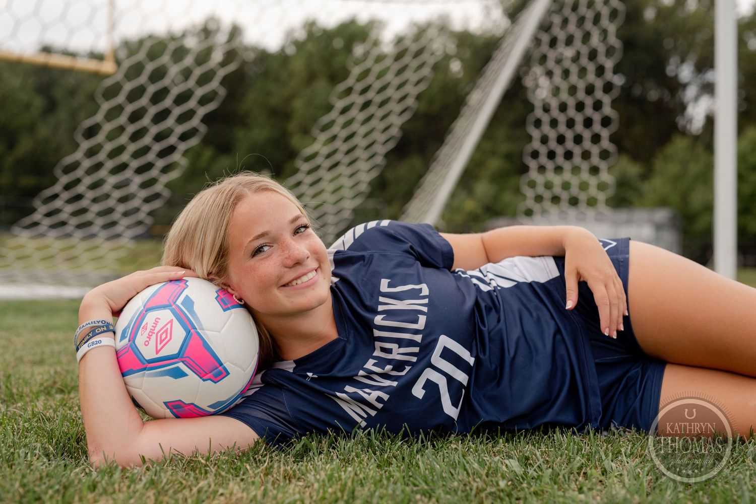 Player in Mavericks uniform lying on grass with soccer ball.
