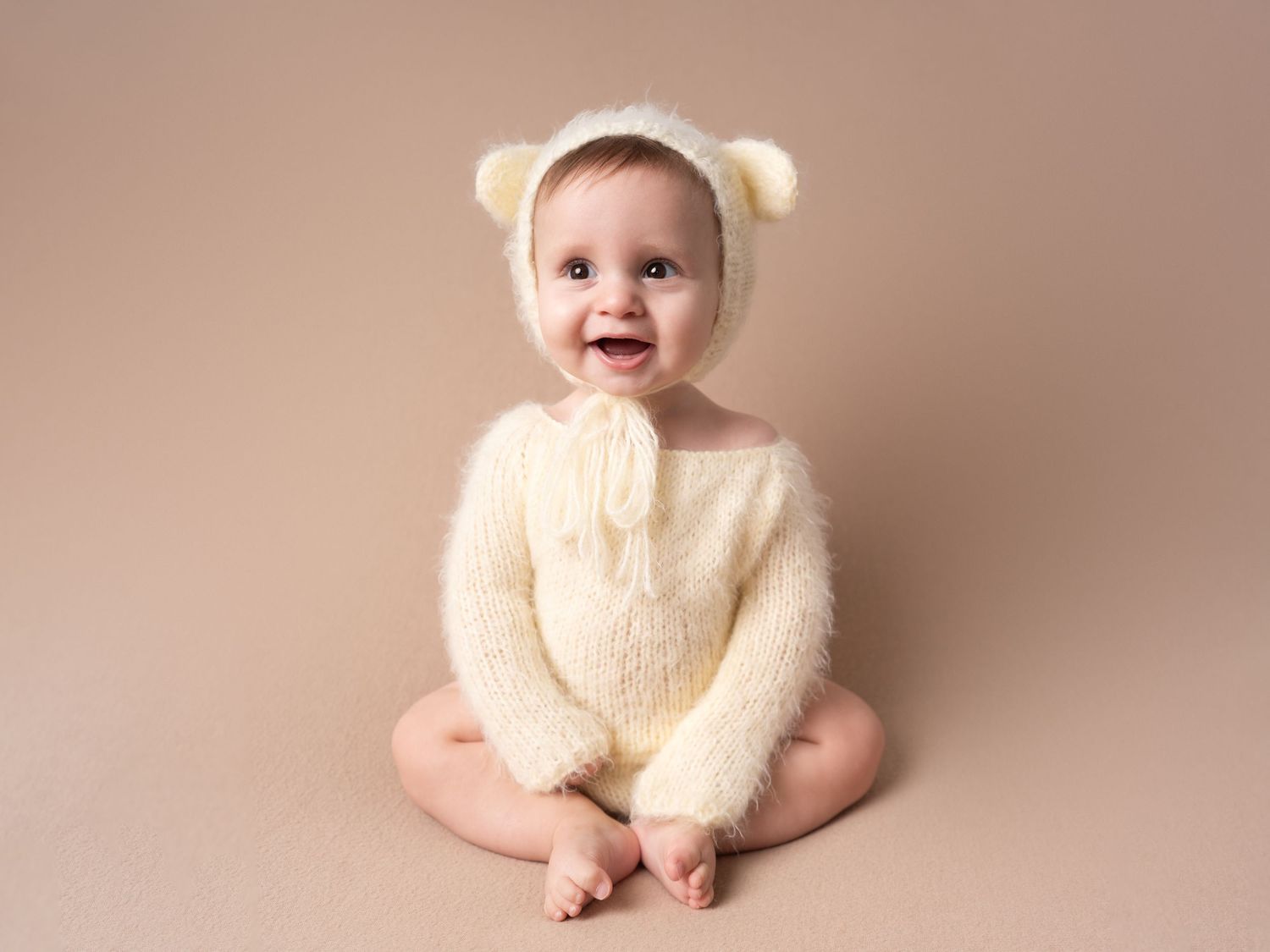 baby boy sitting and smiling in teddy bear romper for sitter session by professional newborn photographer in Doncaster.