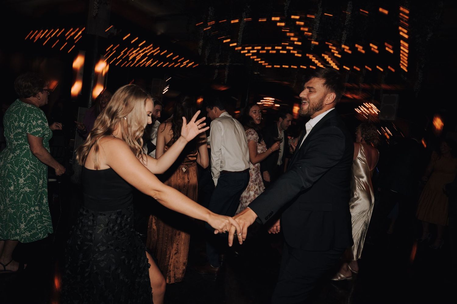 Partygoers dancing together at a dimly lit reception with warm lighting and festive atmosphere.