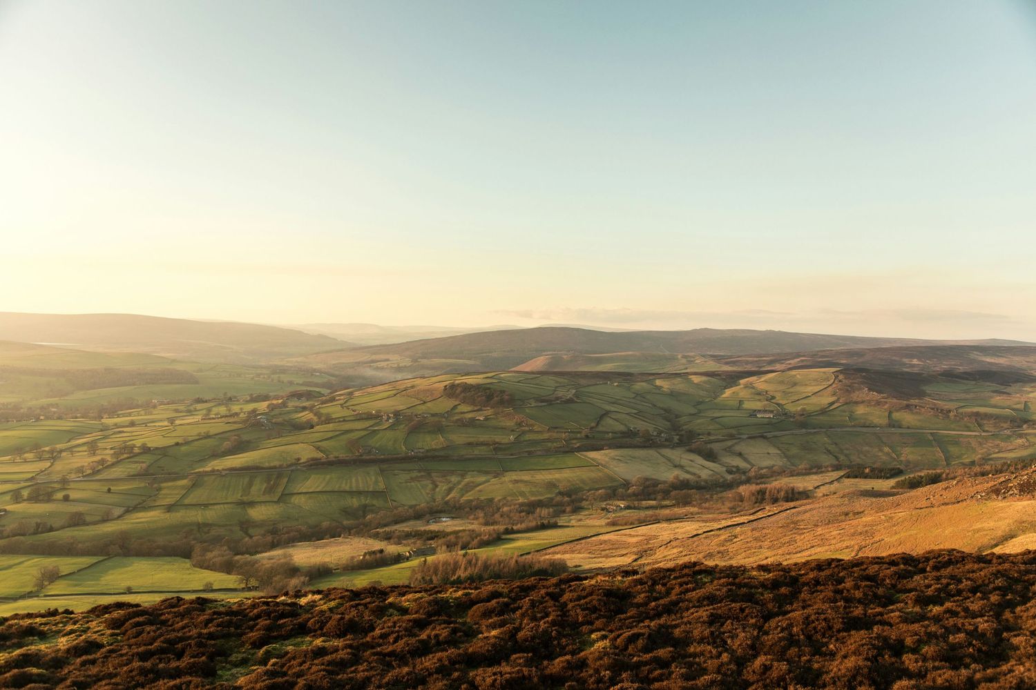 Rolling green hills and valleys stretch into the distance under a soft sunset sky.