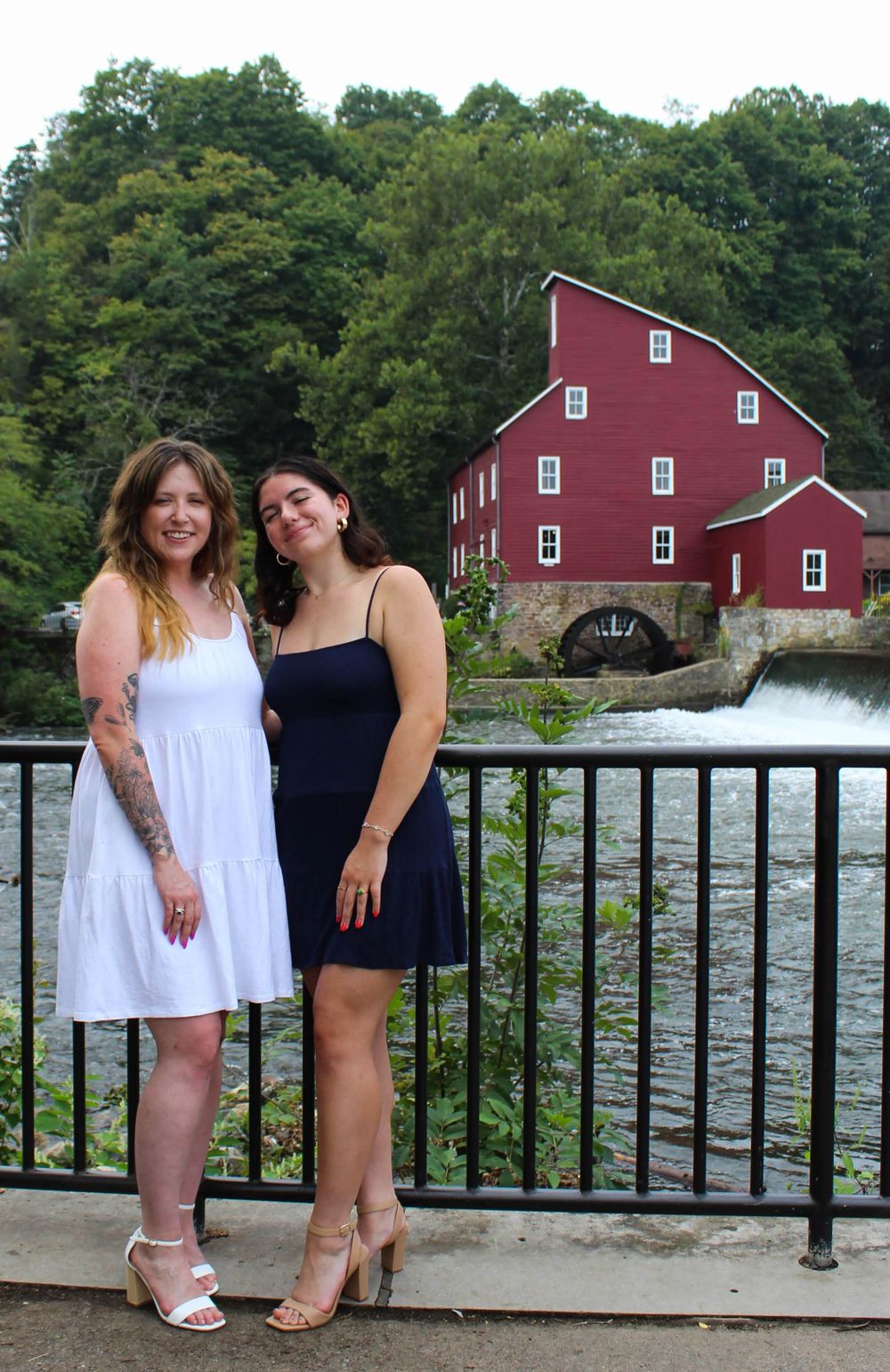 Two people pose by railing with historic Red Mill and waterfall in Clinton, New Jersey.