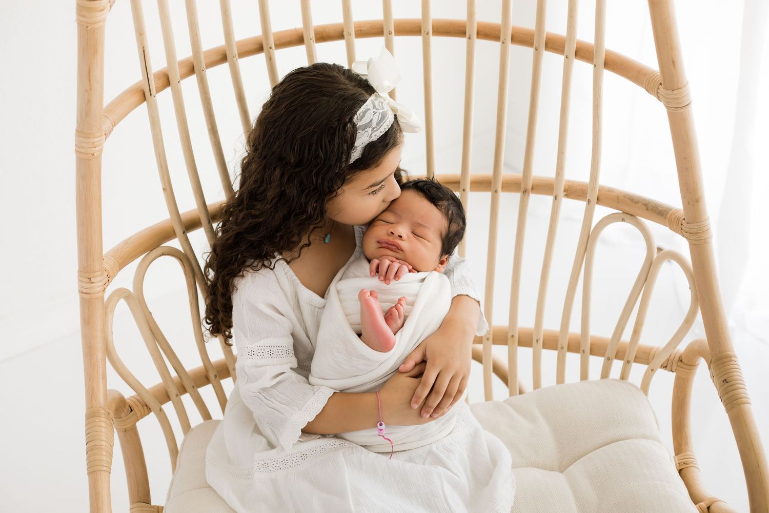 Big sister holds newborn baby for a lifestyle studio session in the white window room for a bright and airy look.