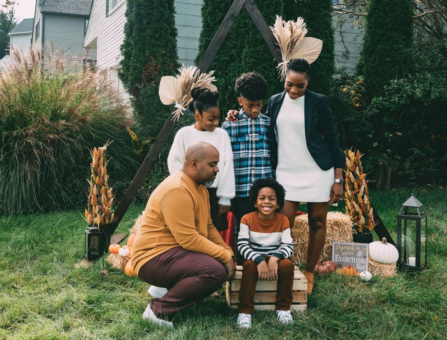 Loving family of five gathers around child seated on wooden crate in festive fall backyard setting.