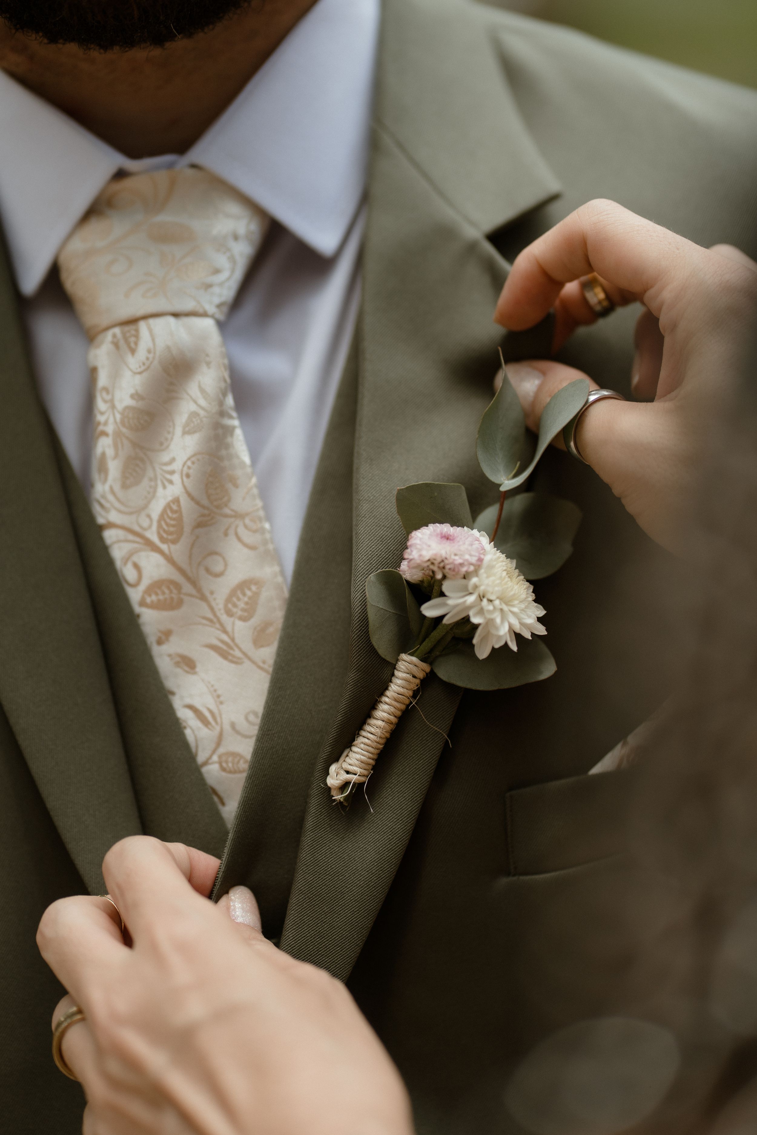 Close-up of hands pinning a white boutonniere onto a gray suit jacket.