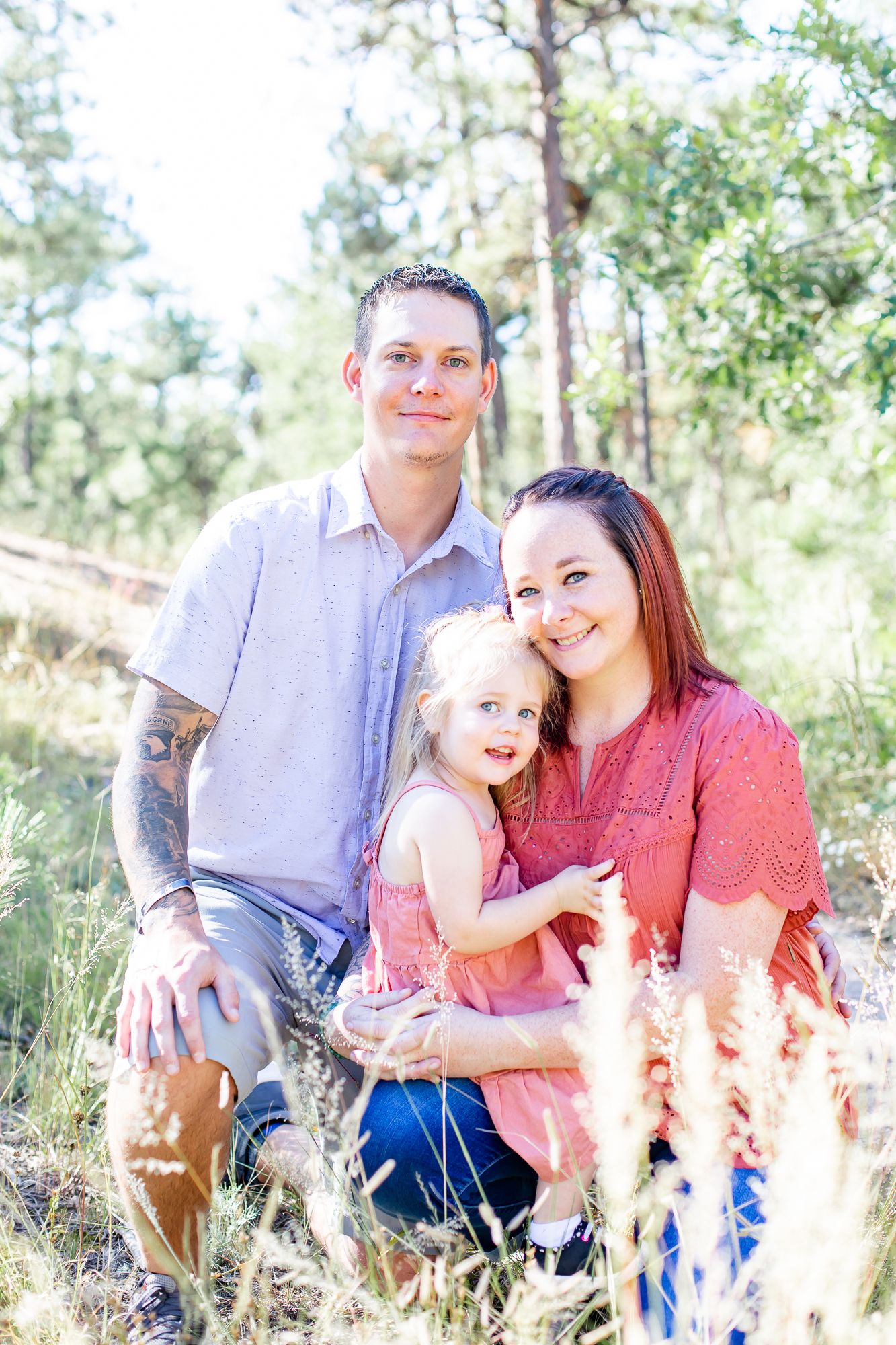 Dad, mom, and their toddler daughter snuggle in the grass in Black Forest, Colorado.
