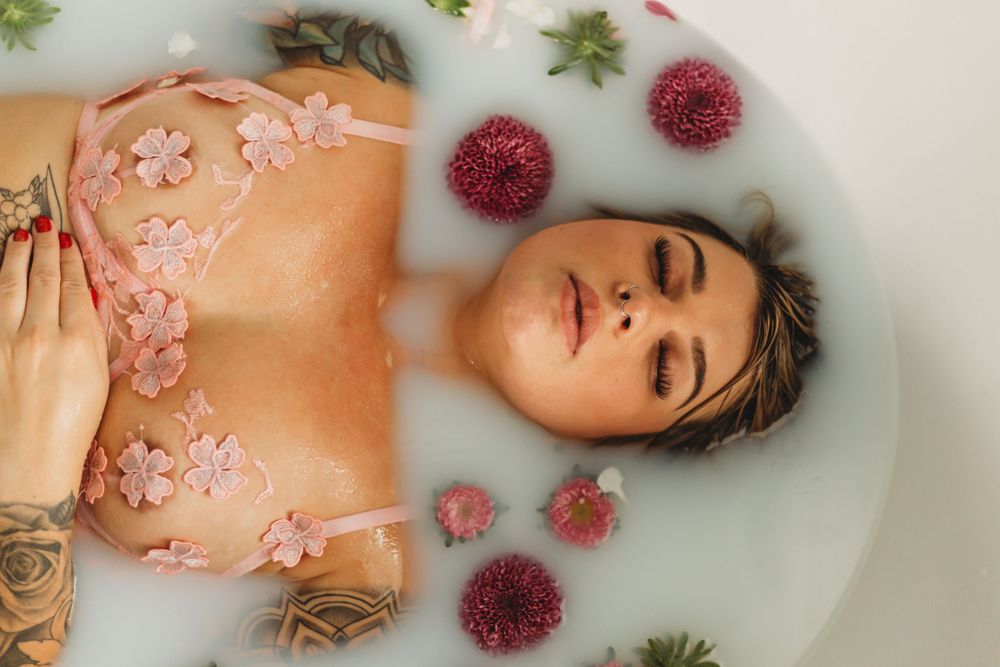 Ethereal overhead milk bath photo with scattered pink petals and burgundy flowers.