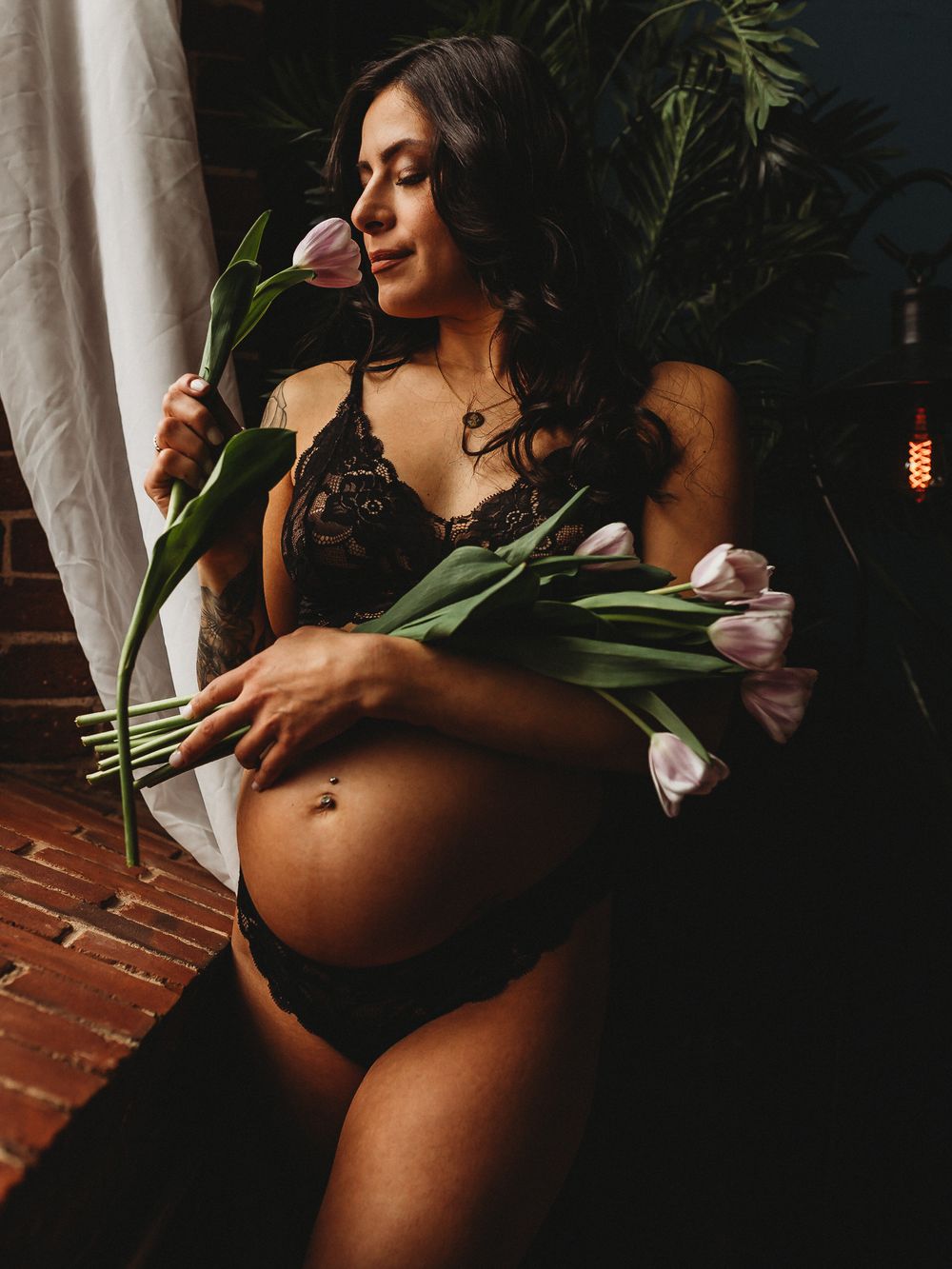 A maternity boudoir photo with lilies and white flowers against a dark moody backdrop.