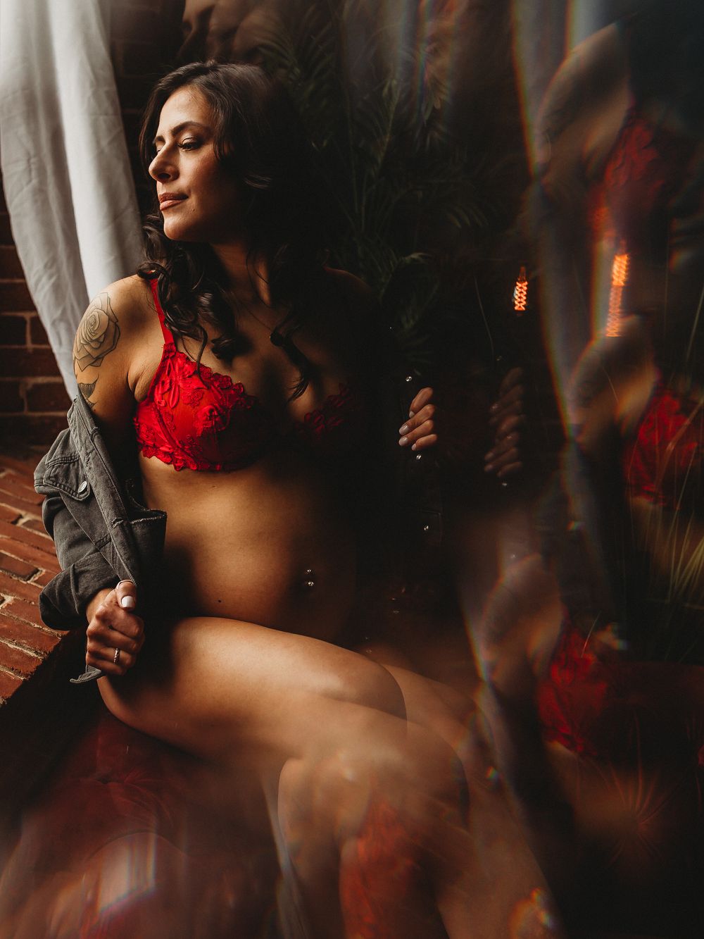 Sensual boudoir portrait with red lingerie in window light against brick wall.
