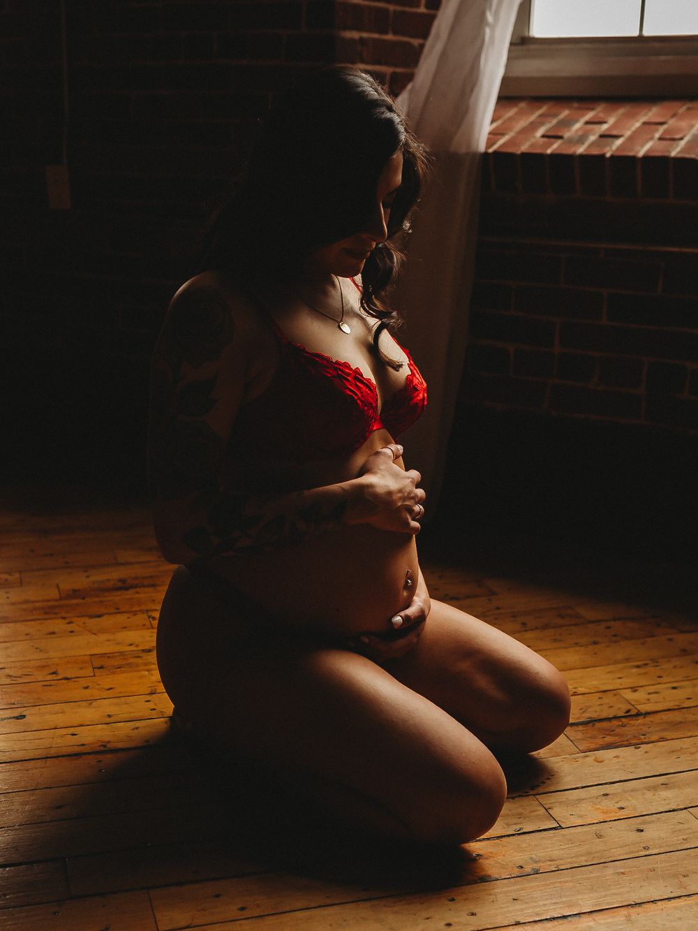 Intimate boudoir photography with moody lighting against brick wall and wooden floor.