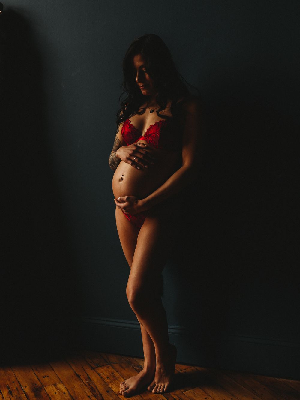 Dramatic maternity portrait in red lingerie against dark background.