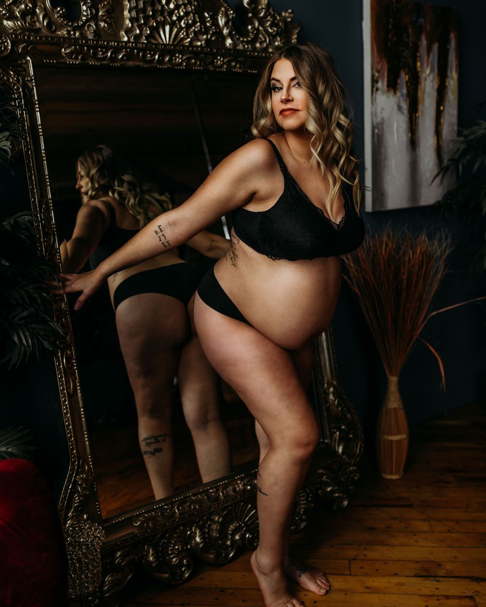 Artistic maternity portrait with pregnant figure posing confidently by decorative mirror.