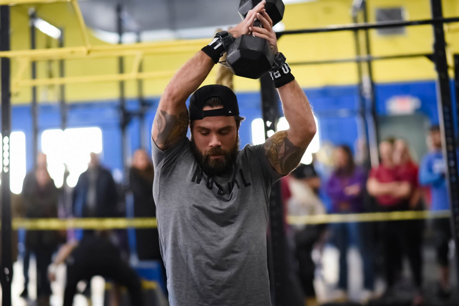 Athlete lifting kettlebell overhead during workout in gym setting.