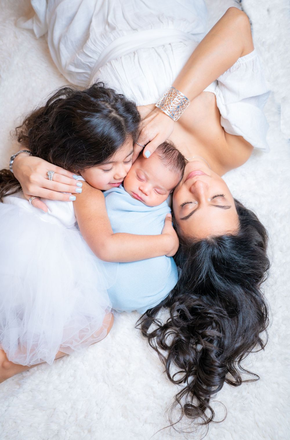Intimate family portrait of mother and child lying on white bedding.