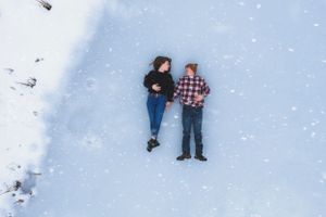 Overhead view of couple lying side by side on snow-covered frozen surface in winter.