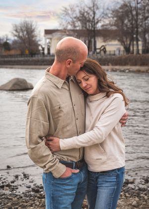 A couple shares a tender embrace near a rocky riverbank at dusk in an outdoor setting.