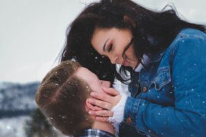 Romantic couple sharing a tender moment in snowy winter landscape, woman leaning in to kiss man.