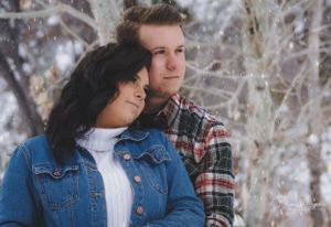 Interracial couple standing together among snow-covered trees in a serene winter outdoor setting.
