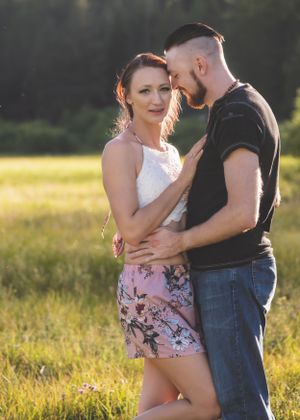 A couple shares an intimate moment embracing in a golden sunlit field with a forest backdrop.