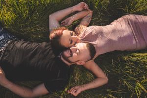 A couple lies in lush green grass facing each other in a peaceful and romantic outdoor setting.