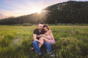 Couple sitting together in a wildflower meadow with a stunning mountain sunset backdrop.