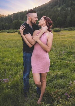 Happy couple embracing and smiling at each other in a lush green mountain meadow at sunset.