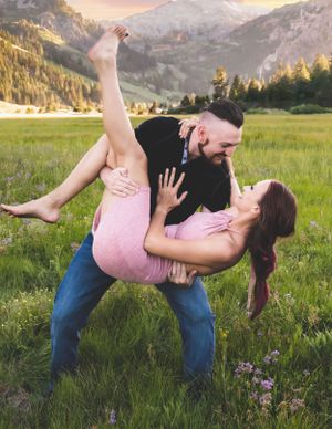 Couple performing a romantic dip pose in a vibrant wildflower meadow with mountain views.