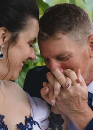 Groom tenderly kissing bride's hand while sharing an intimate moment on their wedding day.