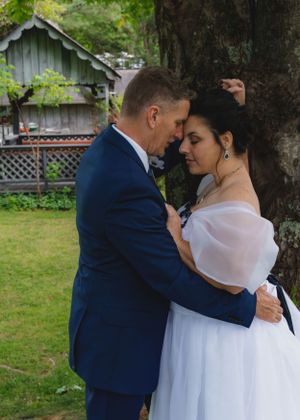 Bride and groom sharing a romantic forehead touch while embracing against a tree in wedding attire.