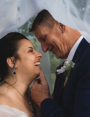 Groom tenderly holding bride's chin under a veil, sharing a loving smile on their wedding day.