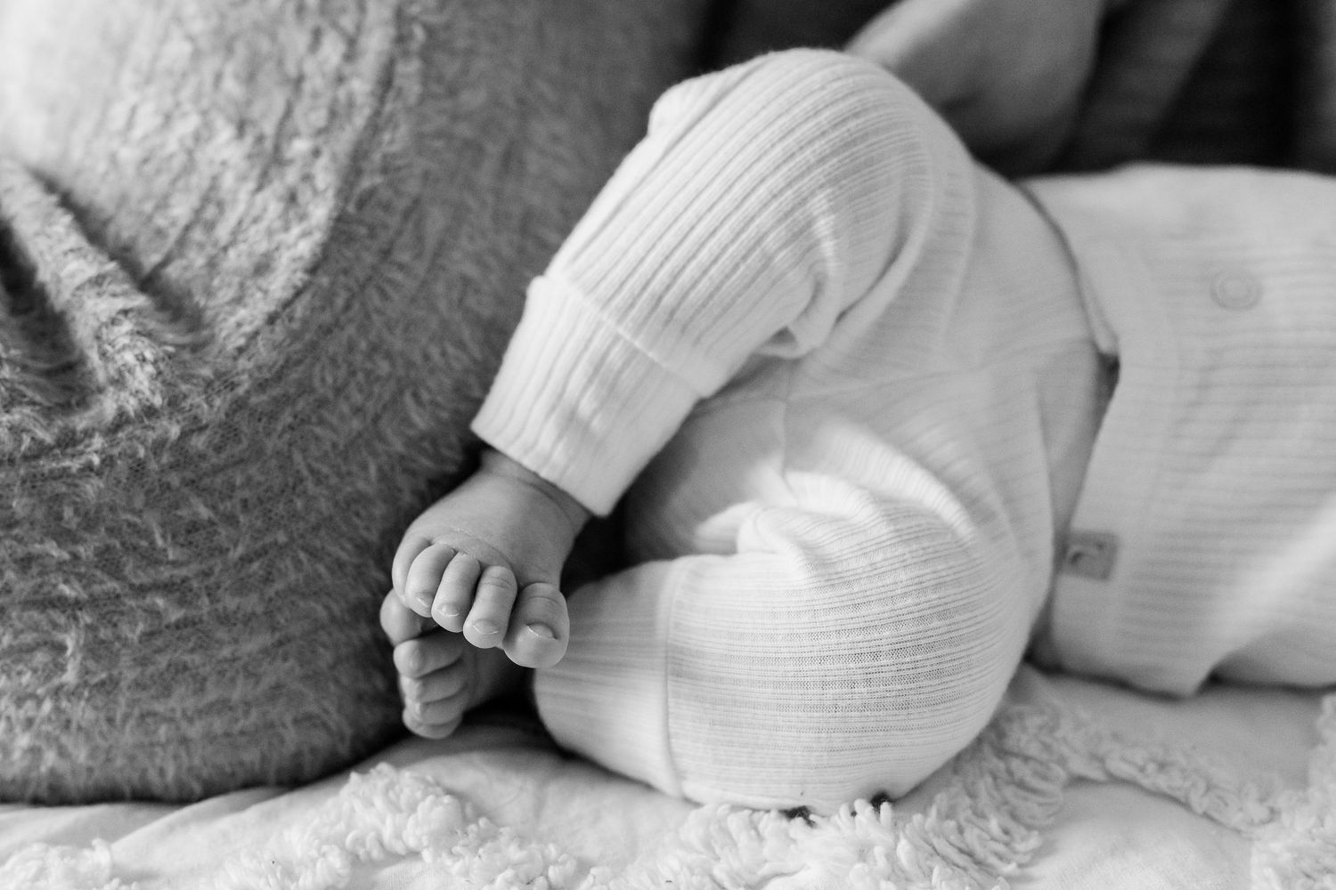 Close up black and white photo of tiny baby feet in white knit clothing on textured bedding.