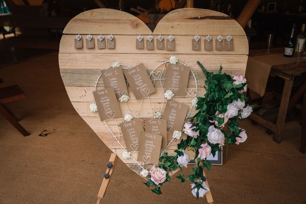 Heart-shaped wooden seating chart with mason jars and floral decorations for wedding table assignments.